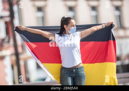 Donna che indossa una maschera facciale tiene dietro di lei una bandiera della Germania. Foto Stock