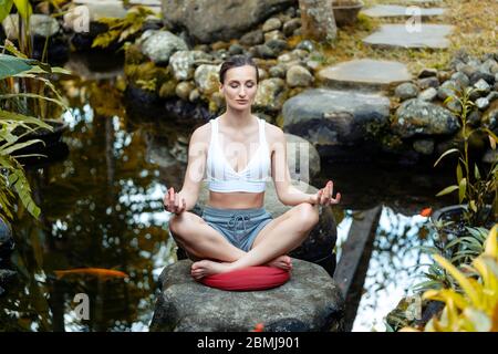 Donna fare yoga a un laghetto con pesci rossi Foto Stock