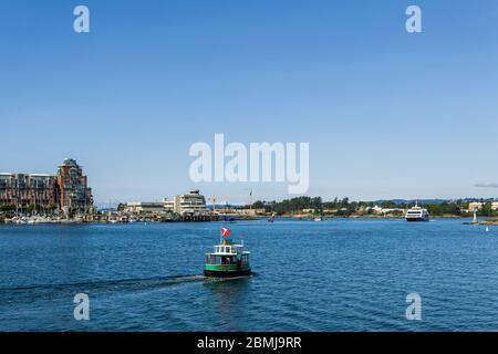 VICTORIA, CANADA - 14 LUGLIO 2019: Autobus verde sul mare nel porto trafficato nella zona del centro con yacht ed edifici moderni. Foto Stock