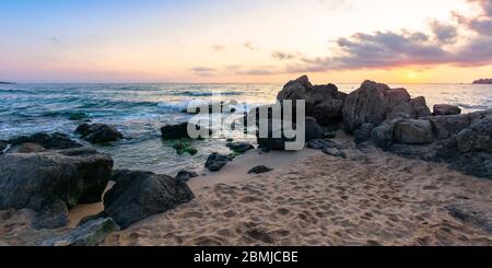 tramonto idilliaco sulla riva del mare. onde che si infrangono sulle rocce sulla spiaggia sabbiosa. bellissimo paesaggio nuvoloso sopra l'orizzonte Foto Stock