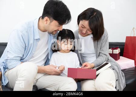 Mamma e papà asiatici stanno disimballando regali con la loro figlia Foto Stock