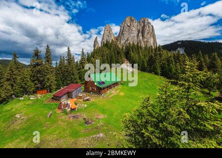 Casa in legno carino sulla tranquilla verde bagliore e Piatra Singuratica scogliere sullo sfondo, Hasmasul Mare montagne, Carpazi, Transilvania, Romania Foto Stock