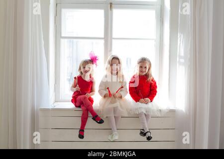 Tre belle ragazze in rosso e bianco vestiti seduta mediante la finestra Foto Stock