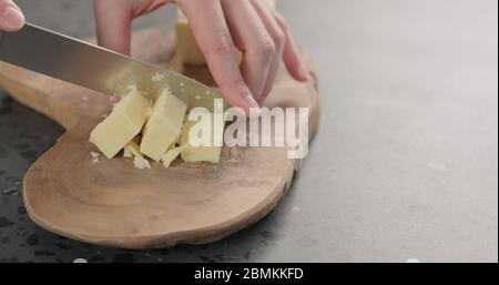 l'uomo ha tagliato a mano il formaggio cheddar a cubetti su legno d'oliva scheda Foto Stock