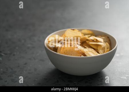 Schegge di patate leggermente cosparse di pepe nero in una ciotola bianca su sfondo concreto con spazio di copia Foto Stock