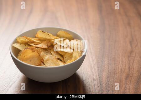 Schegge di patate leggermente cosparse di pepe nero in una ciotola bianca su sfondo in legno di noce con spazio copia Foto Stock