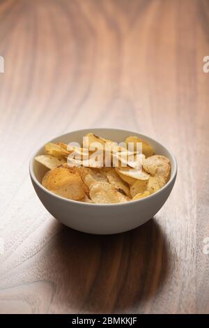 Schegge di patate leggermente cosparse di pepe nero in una ciotola bianca su sfondo in legno di noce con spazio copia Foto Stock