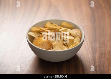 Schegge di patate leggermente cosparse di pepe nero in una ciotola bianca su sfondo in legno di noce con spazio copia Foto Stock