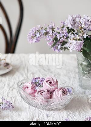 Viola dolce fatto in casa Zephyr o Marshmallow da ribes nero vicino a fiori lilla in vaso di vetro su panno da tavolo bianco Foto Stock
