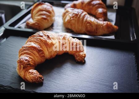 Croissant appena sfornati su piastra di pietra nera e vassoio nero Foto Stock