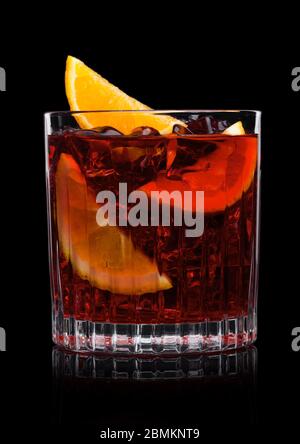 Cocktail Negroni in vetro cristallo con cubetti di ghiaccio e fette di arancia su sfondo nero. Foto Stock