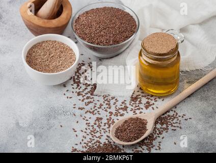Ciotola di semi di lino naturale organico grezzo con cucchiaio e olio di vaso di vetro su sfondo leggero con tela di lino. Semi misti in polvere in ciotola bianca. Foto Stock