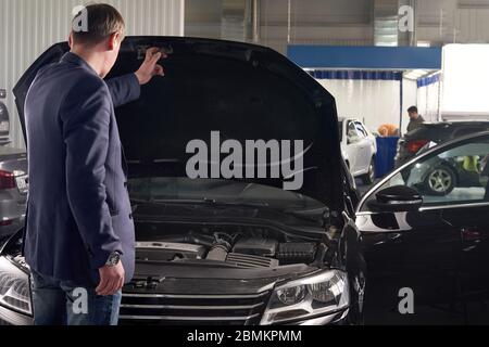 Uomo che guarda il motore di una macchina con cofano aperto Foto Stock