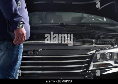 Uomo che guarda il motore di una macchina con cofano aperto Foto Stock