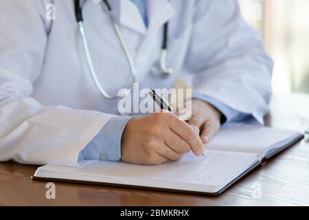 Primo piano di maschio prendere appunti nel giornale medico Foto Stock
