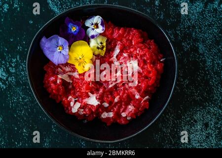 Risotto di barbabietole con fiori commestibili e Parmigiano Reggiano a base di barbabietole biologiche in ciotola in ceramica nera. Cibo biologico sano. Foto Stock