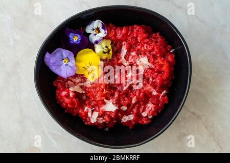 Risotto di barbabietole con fiori commestibili e Parmigiano Reggiano a base di barbabietole biologiche in ciotola in ceramica nera. Cibo biologico sano. Foto Stock