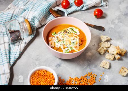 Deliziosa zuppa di lenticchie con panna pesante su tavolo di cemento con peperone rosso, pane tostato. Foto Stock