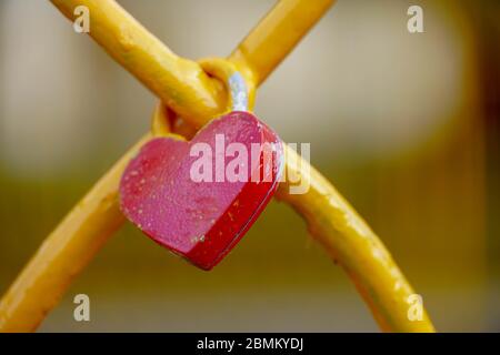 Lucchetto rosso a forma di cuore. Cuore metallico sulla recinzione. Simbolo di amore, concetto romantico. Foto Stock