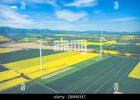 Vista aerea della turbina eolica. Fioritura di colza. Mulini a vento e i campi gialli di cui sopra. Campi agricoli in un giorno d'estate. Fonti di energia rinnovabili. Foto Stock