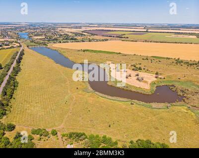 Veduta aerea di una stretta strada di campagna asfaltata grigia, che attraversa un paesaggio con campi. Foto Stock