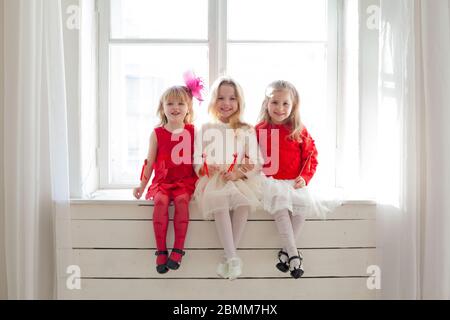 Tre belle ragazze in rosso e bianco vestiti seduta mediante la finestra Foto Stock