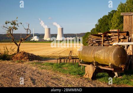 Un melo e vecchie macchine agricole in primo piano di una centrale nucleare, contrasto tra natura e danni ambientali. Foto Stock