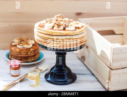 Una pila di frittelle soffici con sciroppo d'acero, banani, marmellata e noci. Rustico sfondo in legno. Tazza di caffè. Foto Stock