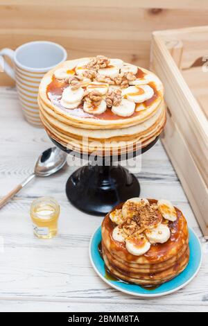 Una pila di frittelle soffici con sciroppo d'acero, banani, marmellata e noci. Rustico sfondo in legno. Tazza di caffè. Foto Stock