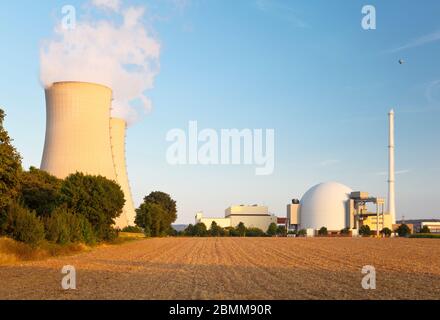 Costruzione di reattori, pila di fumo e due torri di raffreddamento di una centrale nucleare, un campo vuoto in primo piano. Foto Stock