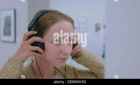 Donna che guarda la esposizione, utilizzando le cuffie e ascolto audio guida in una moderna galleria fotografica. Istruzione e concetto di intrattenimento Foto Stock