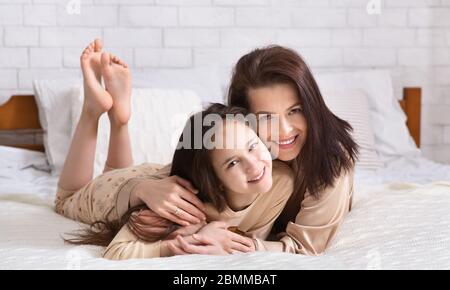 Amore del bambino del genitore. Giovane donna abbracciando la figlia adolescente a letto, panorama Foto Stock