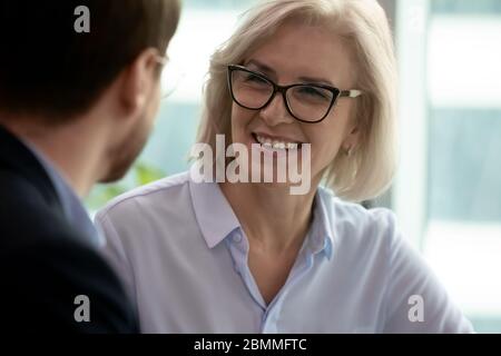 Donna d'affari di mezza età che parla con il partner durante una riunione in ufficio Foto Stock
