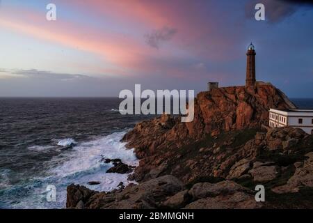 Faro di Cabo Vilan sulla costa galiziana in un tramonto colorato e con il mare in una rabbia. Il faro elettrico più antico della Spagna. Galicia, Spa Foto Stock