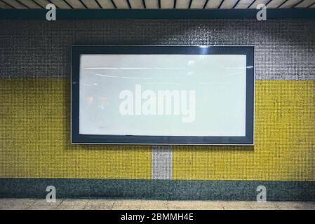 Cartelloni bianchi vuoti su una parete di colore giallo e grigio nei corridoi della metropolitana Foto Stock