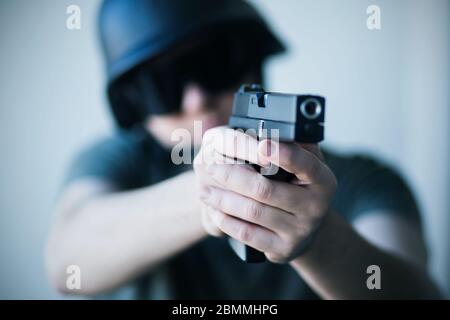 Un uomo in un casco e occhiali protettivi neri tiene una pistola nelle sue mani e prende il mira. Polizia. Esercito. Criminalità. Foto Stock