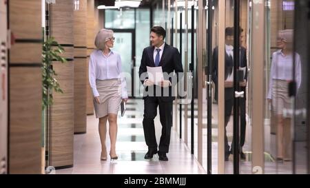 Colleghi che camminano nel corridoio dell'ufficio mentre si intrattenete una conversazione di lavoro Foto Stock