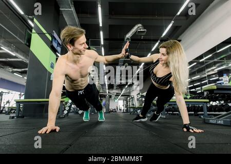 Coppia facendo pushups all'addestramento in palestra. Giovane coppia sportiva che si allena insieme in palestra . Facendo le esercitazioni della plancia mentre tenente l'un l'altro per uno Foto Stock