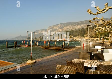 Vista panoramica sul lungolago con una caffetteria vuota in una giornata ventosa con onde alte, Garda, Verona, Veneto, Italia Foto Stock