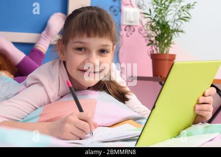 La ragazza studia felice a distanza a casa, si trova a letto e guardato gioiosamente nella cornice Foto Stock