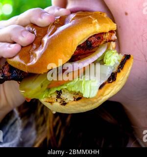 Anonimo giovane donna mangiare UN gustoso hamburger di pollo fresco in UNA brioche tostata Bun Foto Stock