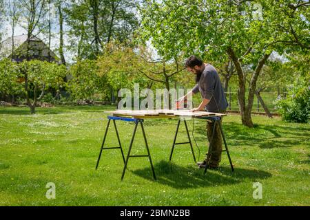 Uomo caucasico medio adulto nel giardino levigare tavole di legno. DIY miglioramento casa, restauro, Falegnameria concetto. Foto Stock