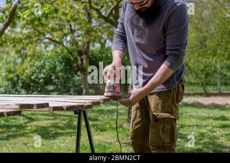 Uomo caucasico medio adulto nel giardino levigare tavole di legno. DIY miglioramento casa, restauro, Falegnameria concetto. Foto Stock