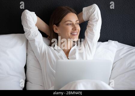 Donna sorridente seduta a letto con notebook al mattino Foto Stock