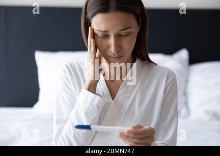 Donna che guarda il test di gravidanza si sente ansioso di cattive notizie Foto Stock