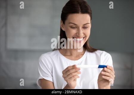 donna 35s che ha tenuto il test di gravidanza ha visto due strisce si sente felice Foto Stock