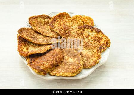 Frittelle di zucchine di verdure servite a forma di sole circolare su piatto bianco su sfondo rustico di legno Foto Stock