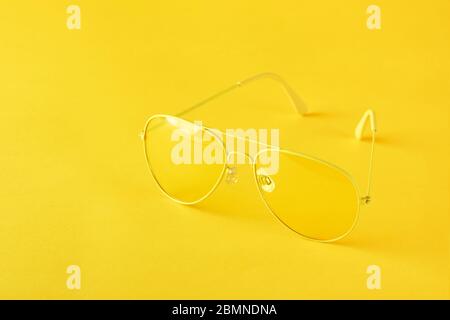 Occhiali da sole moderni aviatori gialli su sfondo di carta gialla. Concetto di protezione solare o estiva. Minimalismo, monocromatico, con spazio per il testo. Foto Stock