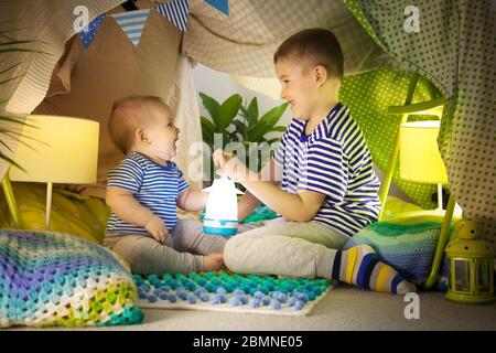 Due carini fratelli giocano con una torcia in una tenda per bambini. bambino di 6 anni e bambino Foto Stock