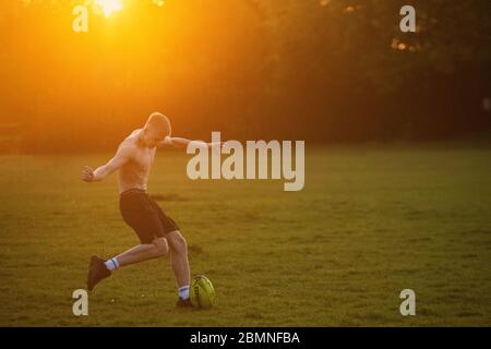 Un teenager muscoloso gioca a rugby al tramonto in un parco londinese Foto Stock